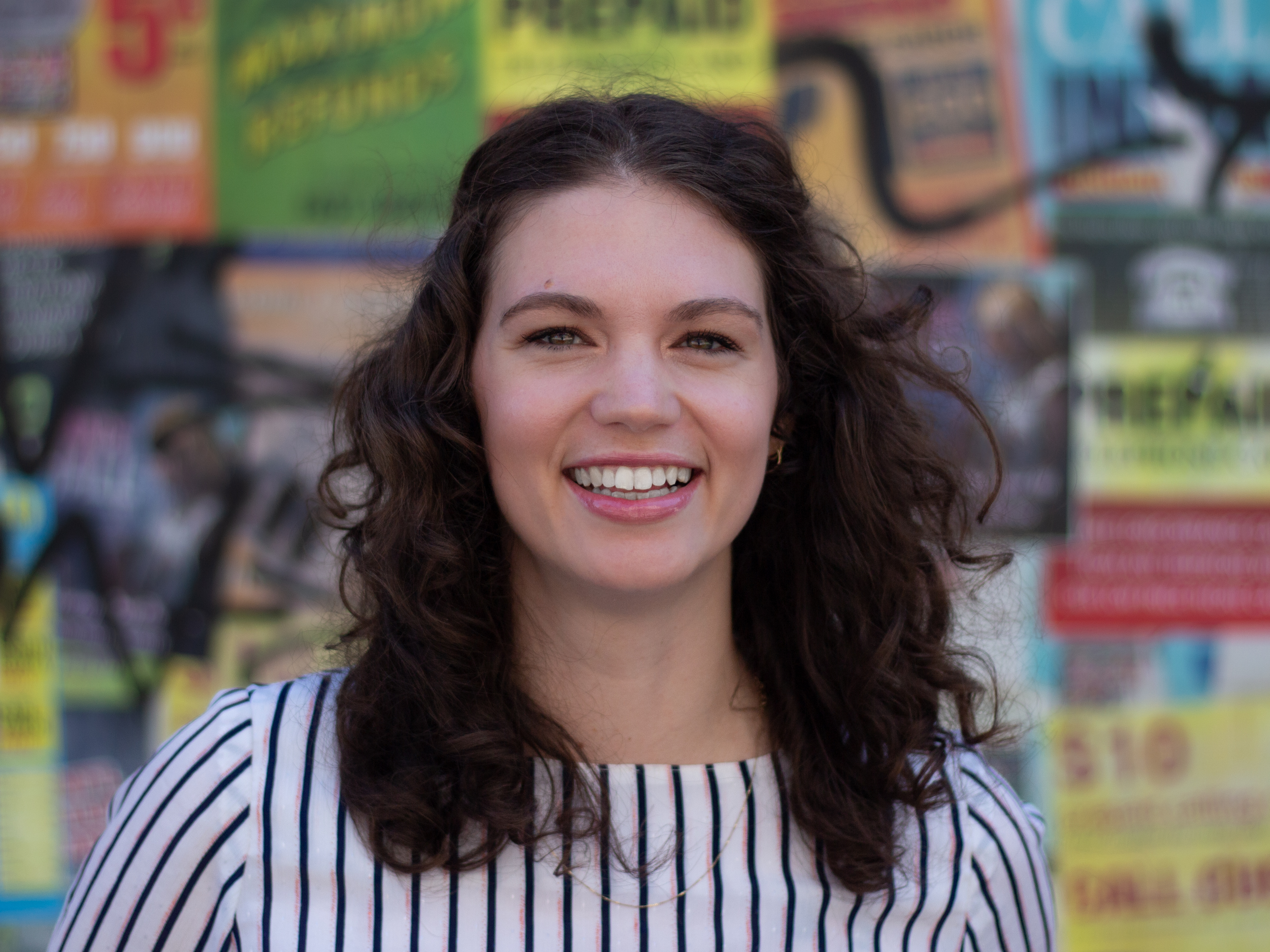 Kaitlin standing alone in front of a graffiti wall smiling